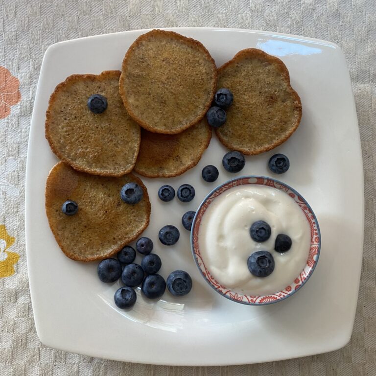Кето блины из миндальной муки и творожного сыра со взбитыми сливками и черникой на белой квадратной тарелке
